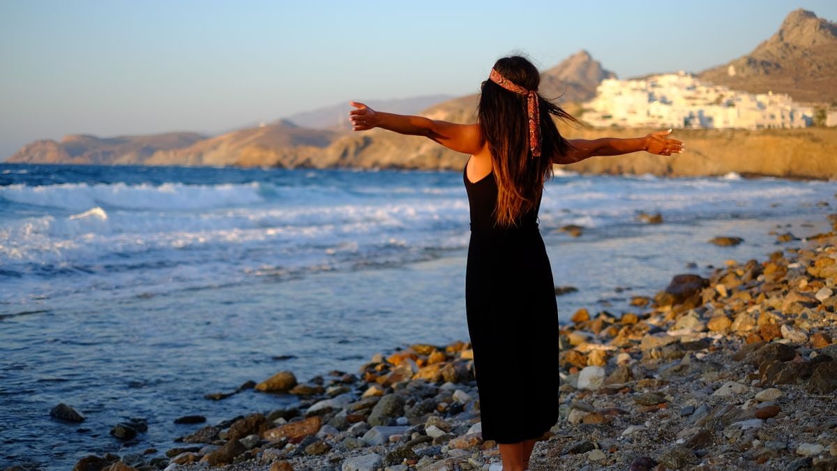 Woman enjoying freedom at sunset on a rocky beach in Greece.
